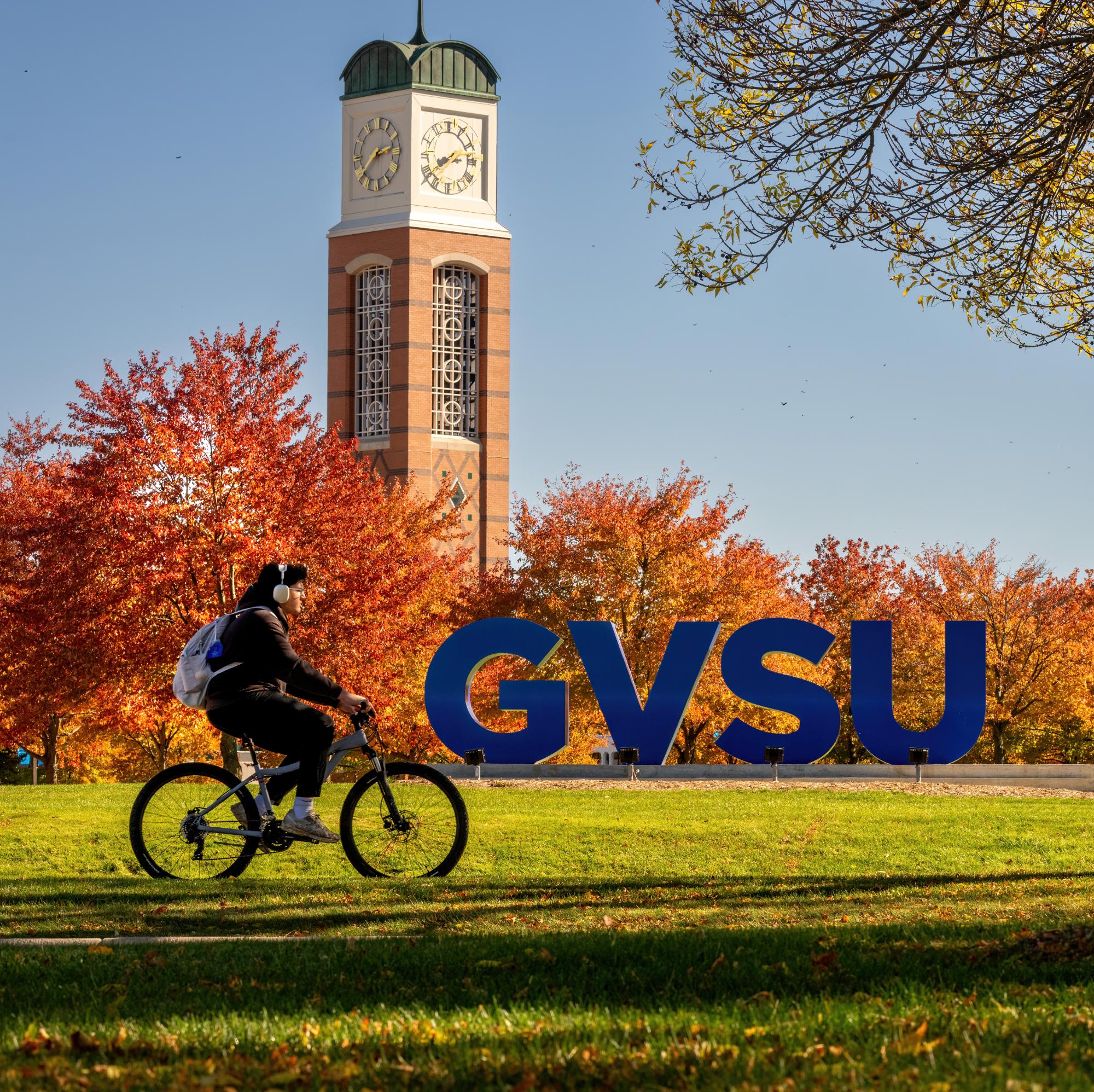 person riding bike on Valley Campus in front of GVSU sign